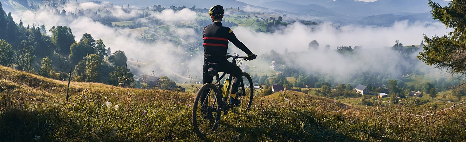 Ein Radfahrer, der von einem Berg hinunter über ein Dorf blickt, welches in dichtem Nebel gehüllt ist